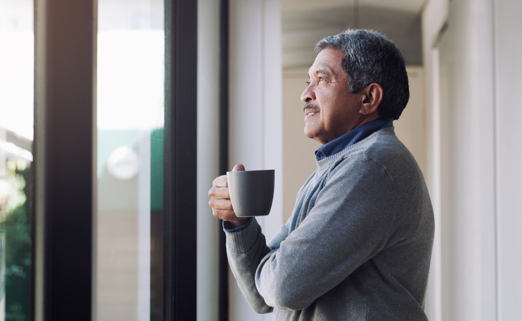 Man looking out window with coffee in hand