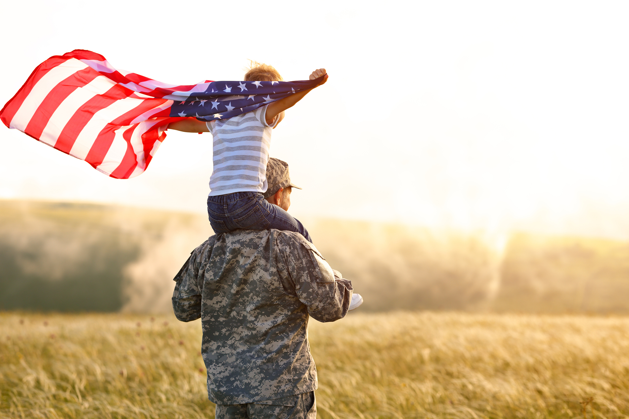Military father and child watching the sunset and flying a US flag