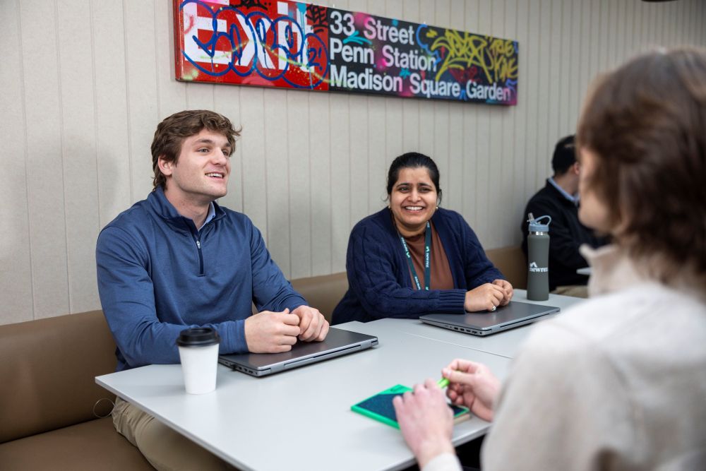 Three coworkers sitting at a table, smiling and talking during a casual meeting.