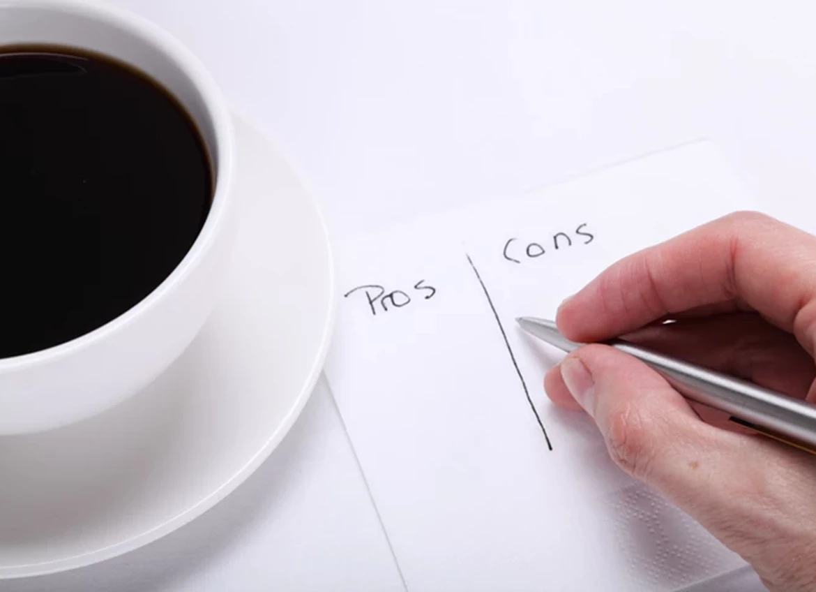 Hand writing pros and cons list next to coffee cup