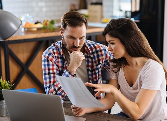 Man and woman looking over a financial sheet sitting at a kitchen table