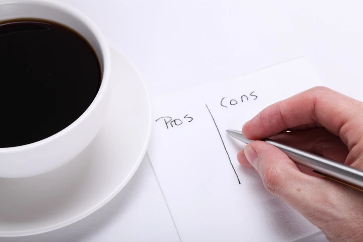 Hand writing pros and cons list next to coffee cup