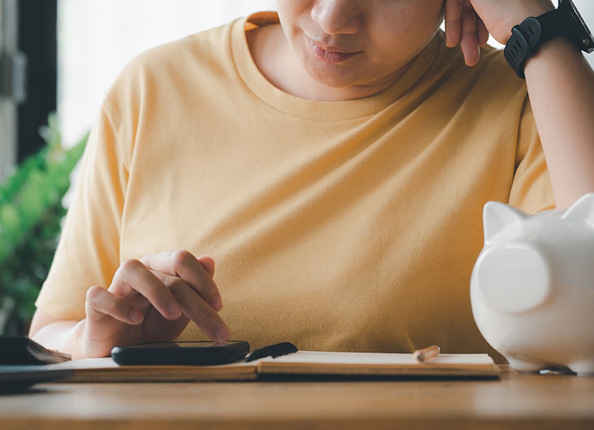 Woman using a calculator sitting at a table with a white porcelain piggy bank