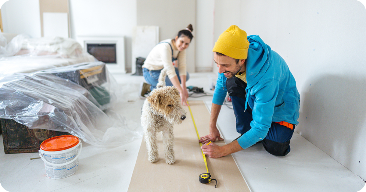 man, woman, and dog using a measuring tape on the floor during renovations